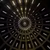 Abstract view of a circular ceiling with rows of vertical light lines converging towards the center, creating a sense of depth. Modern architectural lighting design resembling a spaceship or futuristic structure.